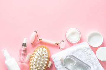 Spa products on pink. Skin care product, cream, soap serum, jade roller and white towel. Flat lay image with copy space.