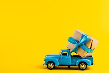 Toy blue car with a gift on a bright yellow background