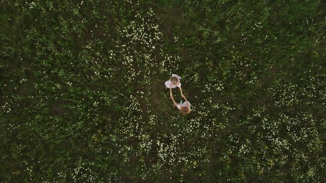 Two young women in summer dresses holding hands and dancing in the field of daises