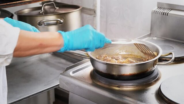 Woman stir frying meat in a pan. Chef hands in gloves cooking chicken liver in cream onion sauce close up. Cook, prepare ingredients for health and diet food delivery in professional restaurant