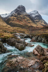 Epic landscape image of vibrant River Coe flowing beneath snowcapped mountains in Scottish Highlands - obrazy, fototapety, plakaty