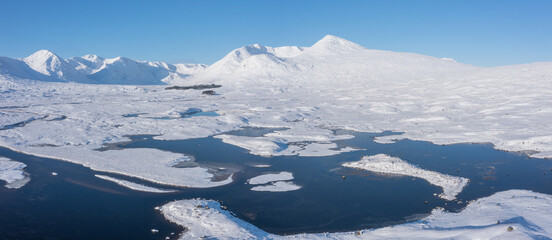 Fototapeta na wymiar Beautiful aerial drone Winter landscape images of Loch Ba and snow covered mountains in background in Scottish Highlands on blue sky Winter day