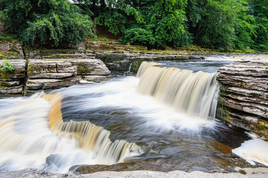 Aysgarth Falls are a three levels one mile stretch waterfalls in Yorkshire Dales National Park, River Ure, Northern England. Long exposure effect photo, selective focus on stones