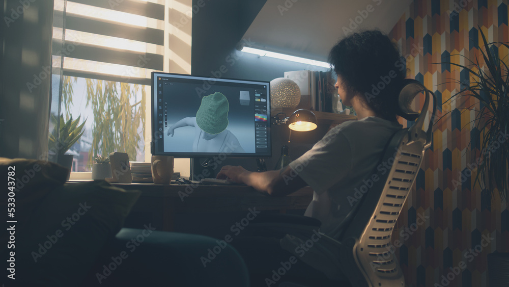 Poster Guy sitting at the table and designing clothes in 3D modeling professional program on personal computer while working remotely from home