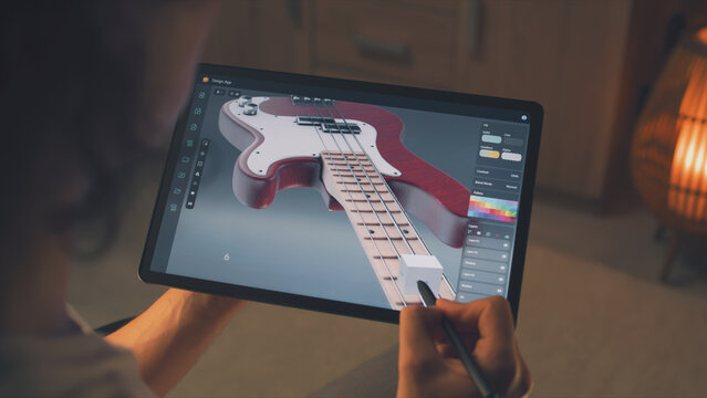 Man working at home remotely and creating 3D prototype of guitar in professional program using digital tablet computer and stylus