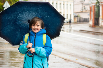 portrait of a smiling schoolboy with an umbrella on a rainy day outside