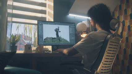 Male 3D designer sitting at the table at home and making animation for video game character, using modern computer and software for creating 3D modeling projects