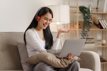 Young happy asian woman using laptop and headphones online meeting with friends via online conference remote meeting.