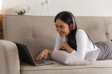 Smiling young asian woman enjoying free time while relaxing with her laptop in living room..