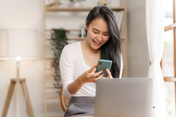 Portrait of smile asian woman freelancer using mobile phone at home office.