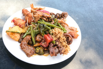 Various Chinese meat and vegetables with fried rice on a white plate and a blue table, copy space, selected focus