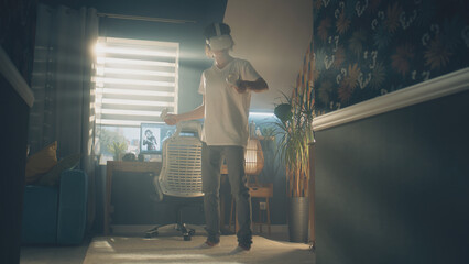 Guy moving while playing video game at home using VR headset and wireless controllers in spare time. Virtual reality device. Cyberspace and metaverse