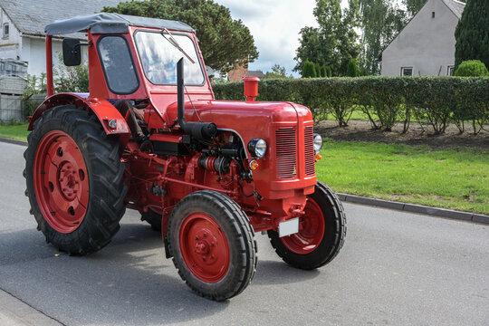 Red vintage tractor, carefully restored oldtimer, driving on the road through the village