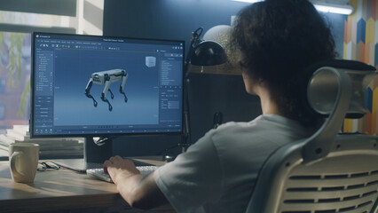 Man sitting at the table and creating 3D prototype of modern robot while working on pc in 3D modeling program remotely from home office - obrazy, fototapety, plakaty
