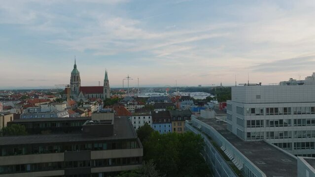 Aerial ascending footage of buildings in urban borough at dusk. Large church and adrenaline attractions on Oktoberfest in distance. Munich, Germany