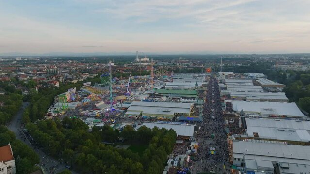 Tourists and locals enjoying attractions of worlds famous fun fair and beer festival. Large tents and amusement park in Oktoberfest area at twilight. Munich, Germany