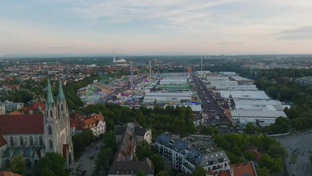 Fly above buildings in urban borough at twilight. Aerial slide and pan footage of crowded Oktoberfest area, famous and popular beer and folk festival. Munich, Germany