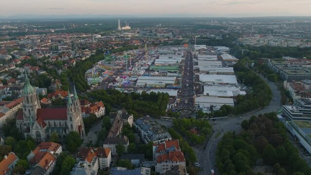 High angle view of Oktoberfest grounds on Theresienwiese, famous beer and folk festival v Bavaria. Backwards reveal of large church and residential buildings. Munich, Germany