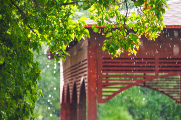 Asian style wooden pergola during rain, sun rays. Sun shower