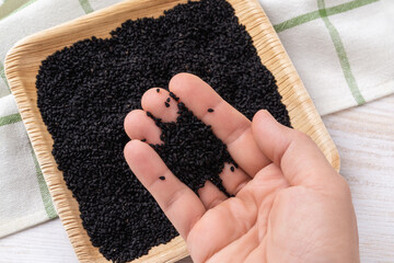Pinch of black cumin seeds on a woman hand palm closeup. Using organic kalonji as spice or seasoning. Cooking with nigella seeds. Nigella sativa for Ayurveda and herbal medicine. - Powered by Adobe
