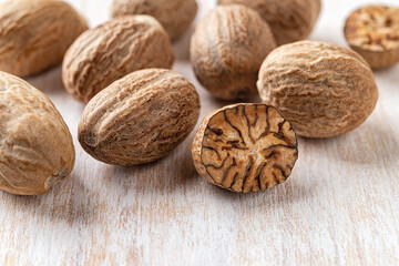 Whole and halved nutmeg seeds over white wooden background macro. Muscat nuts for spice and seasoning concept. Dry fruits of myristica fragrans tree for Ayurveda and herbal medicine.