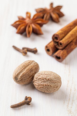 Whole nutmeg seeds, few cloves, star anise, and cinnamon sticks over white wooden background. Spices for autumn pumpkin pie macro. Cooking fall dishes. Spice concept. Vertical frame.