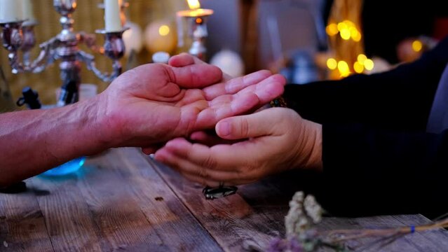 magic session, Female Fortuneteller or esoteric Oracle sees future by reading lines of male client's hand, ritual of healing, candles are burning, incense is being smoked, palm reading