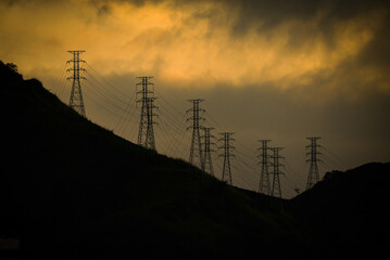 Silhouette of electrical pylons at sunset on the hills above the Zona Norte, or North Zone of Rio de Janeiro, Brazil - obrazy, fototapety, plakaty