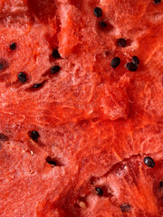 Red watermelon texture with black grains, vertical photo. Tasty natural food, design for background, refreshing summer eating. Closeup, colorful shot, sweet food