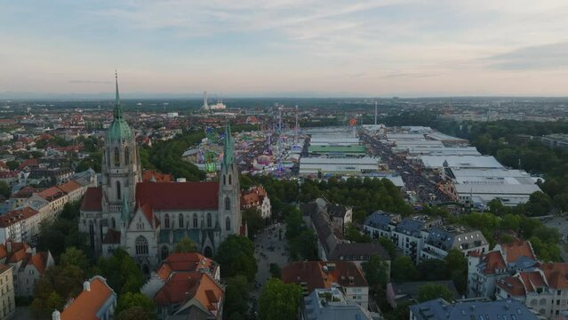 Fly above city at dusk. Slide and pan footage of St. Pauls church and Oktoberfest site on Theresienwiese. Famous and well attended beer festival. Munich, Germany