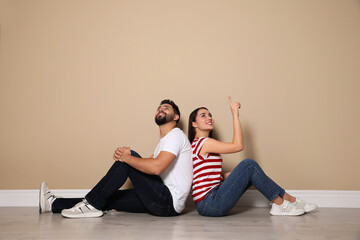 Fototapeta na wymiar Young couple sitting on floor near beige wall indoors