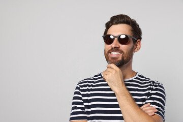 Obraz premium Portrait of smiling bearded man with stylish sunglasses on light grey background. Space for text