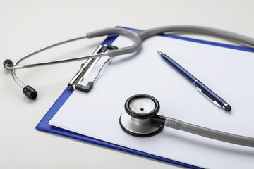 Stethoscope and clipboard on beige background, closeup