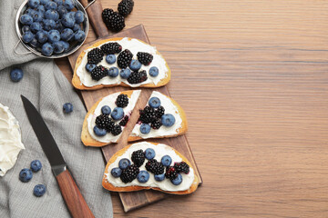 Obraz na płótnie Canvas Tasty sandwiches with cream cheese, blueberries and blackberries on wooden table, flat lay. Space for text