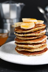 Plate of banana pancakes with honey and powdered sugar on black table, closeup