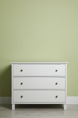 Modern white chest of drawers near light green wall indoors