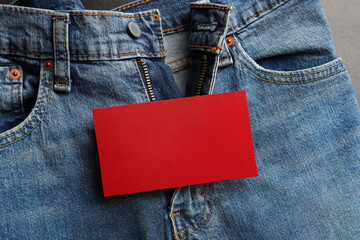 Blue jeans with unbuttoned fly and red blank card on grey background, top view. Exhibitionist...