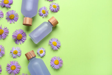 Flat lay composition with bottles of essential oil and daisy flowers on light green background....