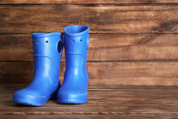 Bright blue rubber boots on wooden surface, space for text