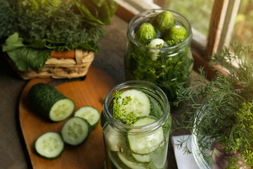 Glass jars, fresh cucumbers and herbs on wooden table indoors. Pickling recipe