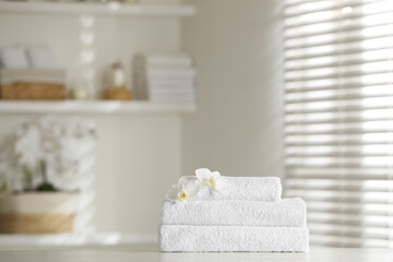 Stack of clean soft towels with orchid flowers on white table indoors
