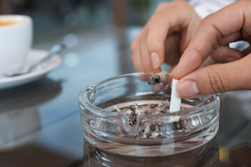 Women putting out cigarettes in ashtray at table, closeup