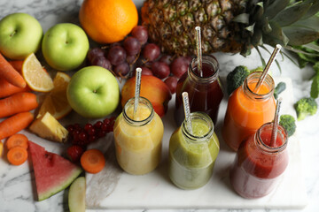Bottles of delicious juices and fresh fruits on white marble table