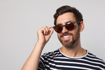 Portrait of smiling bearded man with stylish sunglasses on light grey background. Space for text