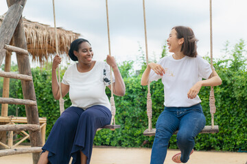 Young African American woman and young Asian woman playing on swing together at the playground. happy holiday travel .