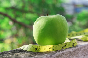 Measure tape and green apple on stone background.