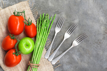 Healthy food vegetable on stone background has asparagus tomato apple fork top view.