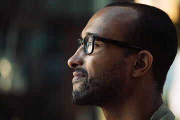 portrait of serious young African man wearing eyeglasses with serious expression in the city, side view