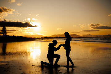 夕日の海辺でプロポーズする男性と受ける女性のシルエット