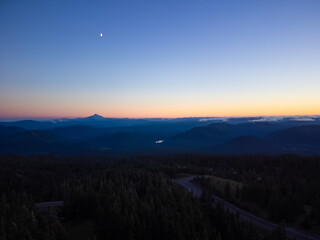 Shooting from the air. Stunning night landscape. Automobile route among the forest and mountains. The sky is colored with orange rays of the setting sun. Tourism, travel, nature.